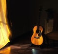 Acoustic Spanish guitar on a stand in the moody shadows of a dark room with bright light coming in from behind a curtain Royalty Free Stock Photo