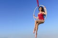 Acrobat athletic, young graceful gymnast portrait on aerial ring outdoors on sky background. flexible woman in red suit performs Royalty Free Stock Photo