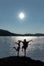 Acrobatic couple in front of sun and lake