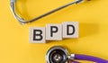 Acronym for BPD (Borderline Personality Disorder) built from blocks of wood on a yellow table with a stethoscope