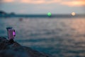 Action camera with luminous pink diode stands on rock over the evening sea. Battery indicator of the device lights up.