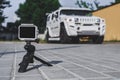 Action camera stands on a tripod on paving slabs. Against the background of a white SUV car