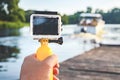 Action camera waterproof with a yellow float in a man`s hand. In the background is a wooden pier with a speedboat on blue water