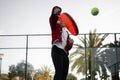 An action shot of a child reaching high to serve a padel tennis ball on an outdoor court, with palm trees in the Royalty Free Stock Photo