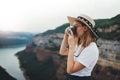 Activ young blonde girl in summer hat takes photo on retro camera of panorama horizin mountain landscape walking on trip outdoors Royalty Free Stock Photo