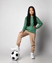 Active Asian kid girl in green sportswear and white sneakers stands with soccer football ball under her foot Royalty Free Stock Photo