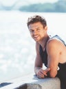 Active athlete muscular young man portrait dressed sleeveless shirt resting after the jogging by the river promenade on the sunny