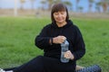 Active beautiful senior woman resting holding water bottle after yoga, work out exercising for health in the park on Royalty Free Stock Photo