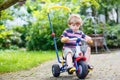 Active blond kid boy driving tricycle or bicycle in domestic gar Royalty Free Stock Photo