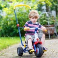 Active blond kid boy driving tricycle or bicycle in domestic gar Royalty Free Stock Photo