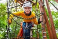 Active brave little boy enjoying climbing at treetop adventure park and smiles