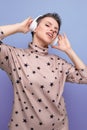 active bright caucasian young woman with a short haircut dressed in a beige suit listens to music in wireless bluetooth