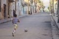 Active Caucasian child kicking ball in a rural Cuban street