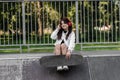 Active child girl with skate board and listen to music with headphones and sitting on skate playground and smile