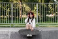 Active child girl with skate board and listen to music with headphones and sitting on skate playground and smile