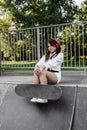 Active child girl with skate board and listen to music with headphones and sitting on skate playground and smile