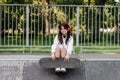 Active child girl with skate board and listen to music with headphones and sitting on skate playground and smile