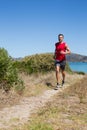 Man running on dirt trail wearing red shirt and running shoes near calm bay, copy space Royalty Free Stock Photo