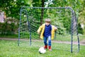 Active cute little kid boy playing soccer and football and having fun, outdoors. Child having game on rainy day. Wearing