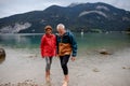 Active elderly couple hiking together in spring mountains, walking in cold water in mountain lake. Senior tourists