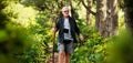 Active elderly man walks with a stick through the green forest, health route. Adventure is ageless