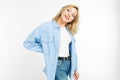 Active emotional blonde girl in jeans and a blue shirt standing against a white wall with copy space