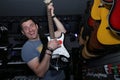 Active emotional with a smile on his face a young man playing an electric guitar against the background of guitars in a soft blur Royalty Free Stock Photo