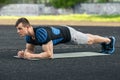 Active fitness man doing planking exercise in the stadium, muscular male workout, outdoors