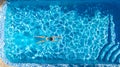 Active girl in swimming pool aerial drone view from above, young woman swims in blue water, tropical vacation