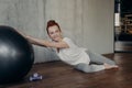 Smiling sportive ginger woman in sportswear laying on wooden floor with silver fitness ball Royalty Free Stock Photo