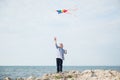 Active happy little boy holding flying colorful kite flying in air standing on rock sea coast on summer sunny day Royalty Free Stock Photo