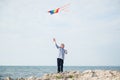 Active happy small boy holding flying colorful kite flying in air standing on rock sea shore on summer sunny day Royalty Free Stock Photo