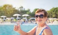 Active senior woman (over age of 50) in swimsuit and sunglasses showing thumbs up on swimming pool background. i Royalty Free Stock Photo