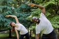 Active healthy couple, African guy and Caucasian girl, working out together outdoors, doing stretching exercises on the