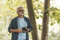 An active hobby of an elderly man with a beard outdoors. A pensioner takes pictures of nature with a camera while traveling