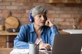 Active latin female retiree in headset confer online using laptop