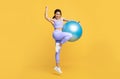 Active lifestyle concept. Overjoyed black woman jumping with fitness ball and celebrating success over yellow background Royalty Free Stock Photo