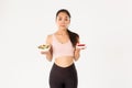 Active lifestyle, fitness and wellbeing concept. Indecisive cute asian slim girl in workout outfit, holding healthy