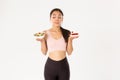 Active lifestyle, fitness and wellbeing concept. Indecisive cute asian slim girl in workout outfit, holding healthy