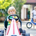 Active little boy driving pedal car in summer garden Royalty Free Stock Photo