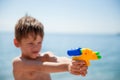 Active little caucasian boy holding water plastic toy gun aiming in target on summer beach Royalty Free Stock Photo