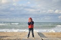 Active little boy in red and blue jacket and hood freeze near stormy sea in autumn weather sunset Royalty Free Stock Photo