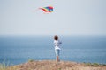 Active little kid holding flying color kite in air above blue ocean and sky in summer leisure games Royalty Free Stock Photo