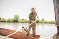 Active male fisher with dog sailing from shore in old boat, going fishing in sunny day.