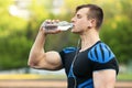 Active man drinking water from a bottle, outdoors. Young fit male quenches thirst