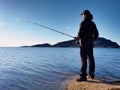 The active man is fishing on sea from the rocky coast. Fisherman check pushing bait Royalty Free Stock Photo