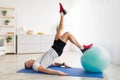 Active mature man exercising with ball, doing abs exercises on mat in living room interior, free space Royalty Free Stock Photo