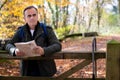 Active Mature Man With Map Resting On Gate Walking Through Autumn Woodland