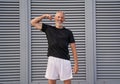 Active mature man in sportswear looking at camera, showing his muscular arm while standing outdoors over gray background Royalty Free Stock Photo