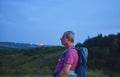 Active middle aged man standing on hill with backpack, enjoy looking at mountains landscape during twilight Royalty Free Stock Photo